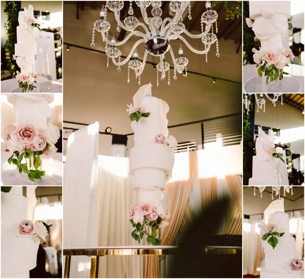 Snohomish Wedding Photographer GSquared Weddings A multitiered white wedding cake with elaborate swirling fondant designs adorned with pink roses The cake is displayed on a reflective table beneath a sparkling crystal chandelier surrounded by draped curtains Serving Seattle Snohomish and Washington State Snohomish Wedding Photographer GSquared Weddings A multi-tiered white wedding cake with elaborate swirling fondant designs, adorned with pink roses. The cake is displayed on a reflective table beneath a sparkling crystal chandelier, surrounded by draped curtains. Serving Seattle, Snohomish and Washington State