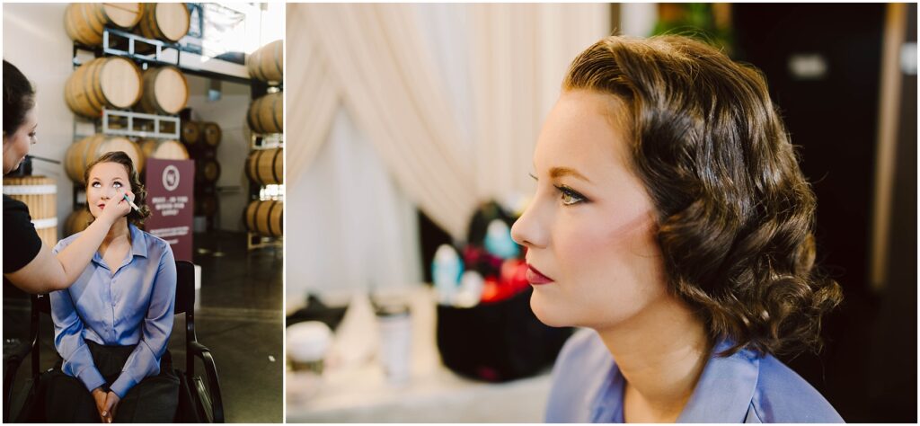 Snohomish Wedding Photographer GSquared Weddings A woman in a blue shirt getting makeup applied by another person. Shes seated indoors, with a background of stacked barrels and a blurred interior setting. Close-up on her face shows elegant makeup and styled hair. Serving Seattle, Snohomish and Washington State
