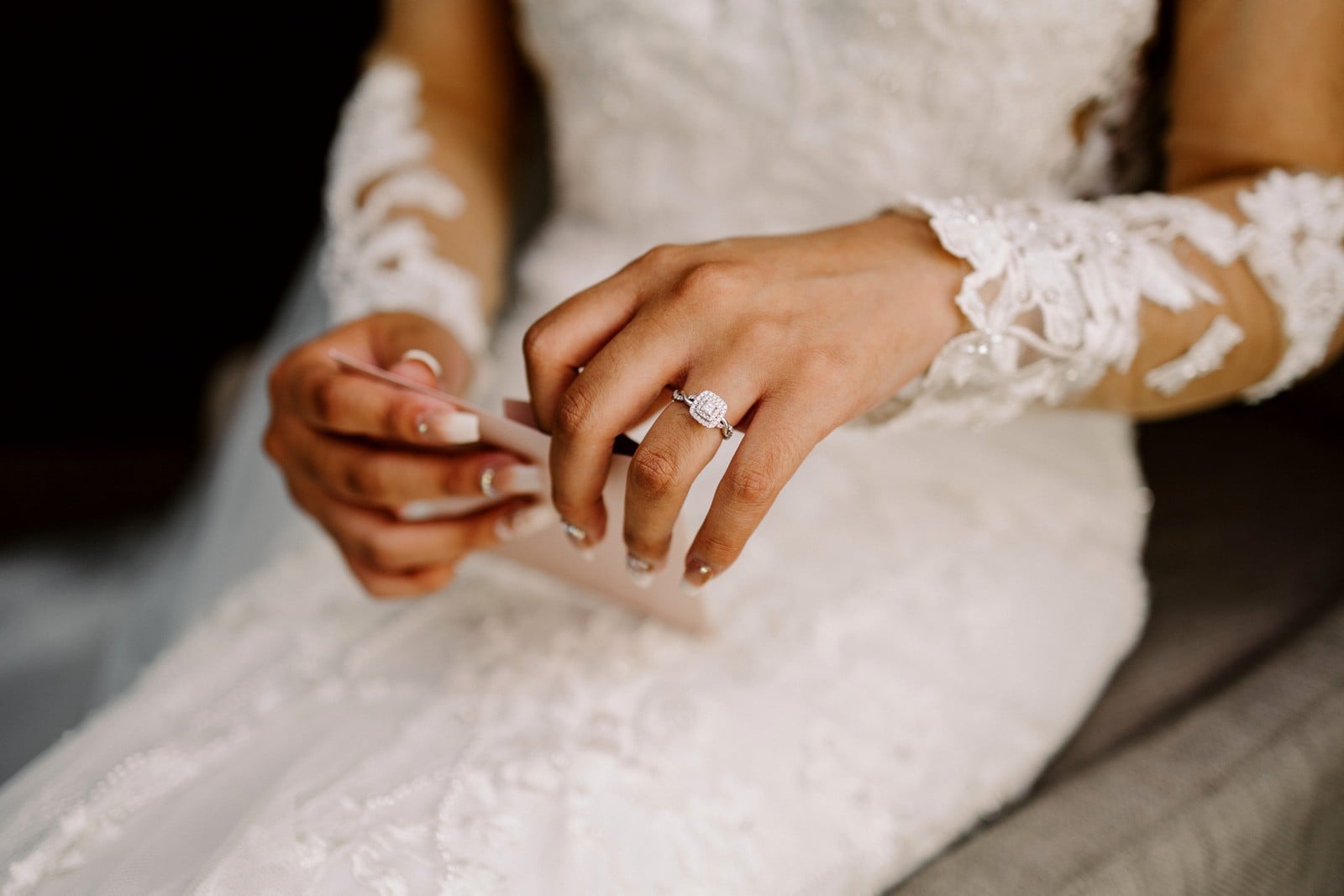 Snohomish Wedding Photographer GSquared Weddings A bride in an intricately detailed lace wedding dress and sheer sleeves holds a folded piece of paper. Her left hand, adorned with a diamond ring, is central in the image, showcasing her elegant manicure. Serving Seattle, Snohomish and Washington State