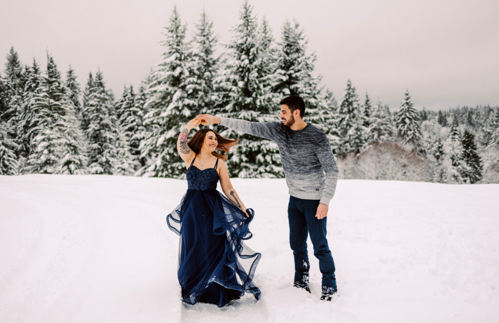 Snohomish Wedding Photographer GSquared Weddings A couple twirls joyfully in a snowy landscape immortalized in stunning photos The woman wears a flowing navy blue gown while the man dons a gray sweater and dark pants Snowcovered trees and a cloudy sky complete the enchanting backdrop Serving Seattle Snohomish and Washington State Snohomish Wedding Photographer GSquared Weddings A couple twirls joyfully in a snowy landscape, immortalized in stunning photos. The woman wears a flowing navy blue gown, while the man dons a gray sweater and dark pants. Snow-covered trees and a cloudy sky complete the enchanting backdrop. Serving Seattle, Snohomish and Washington State