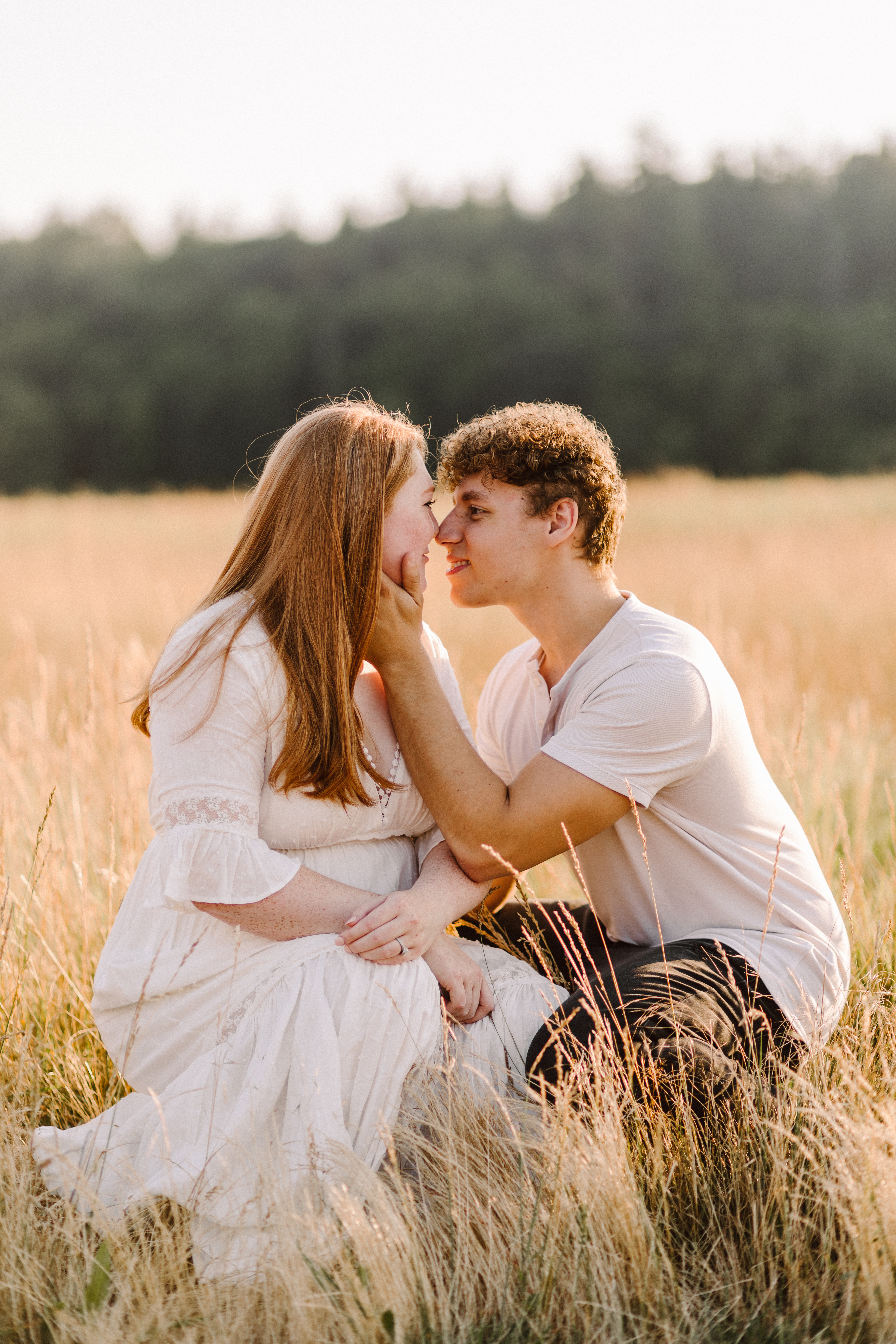 Snohomish Wedding Photographer GSquared Weddings A couple poses for photos in a sunlit field of tall grass The woman with long auburn hair wears a white dress while the man in a light shirt gently holds her face They gaze at each other with trees blurred in the background Serving Seattle Snohomish and Washington State