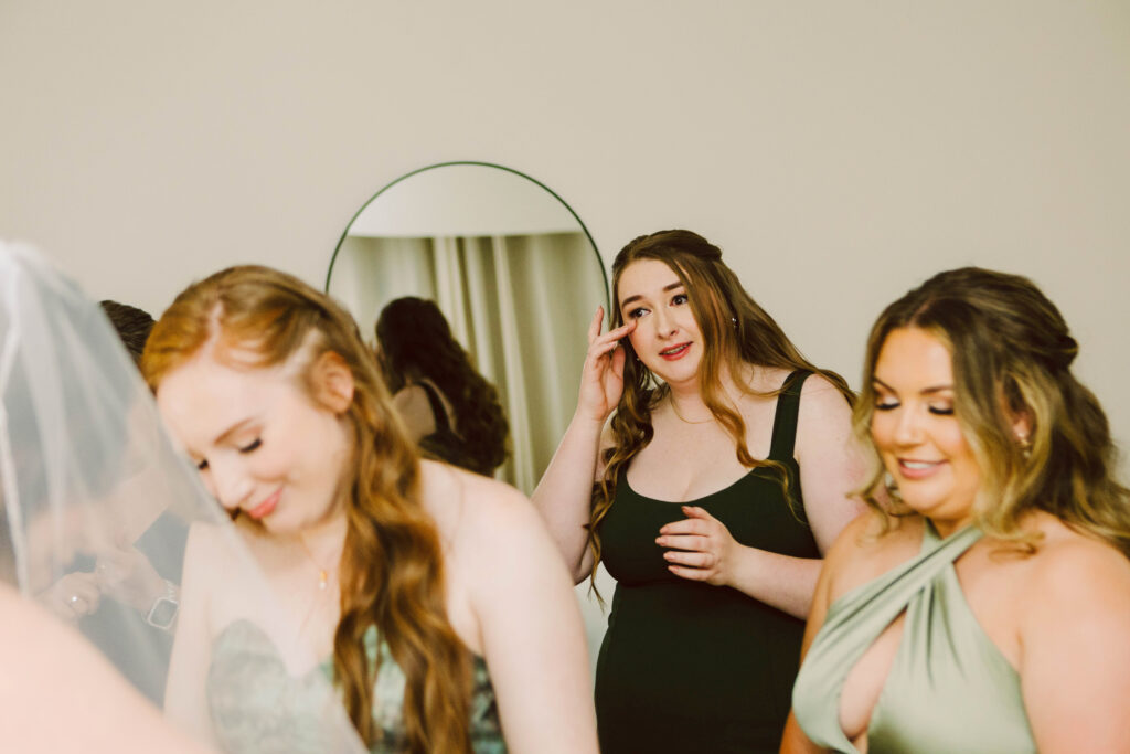 Snohomish Wedding Photographer GSquared Weddings A group of women preparing for a wedding One woman wipes her eye while others dressed in elegant attire smile gently A mirror in the background reflects part of the scene The atmosphere is warm and anticipatory Serving Seattle Snohomish and Washington State Snohomish Wedding Photographer GSquared Weddings A group of women preparing for a wedding. One woman wipes her eye, while others, dressed in elegant attire, smile gently. A mirror in the background reflects part of the scene. The atmosphere is warm and anticipatory. Serving Seattle, Snohomish and Washington State