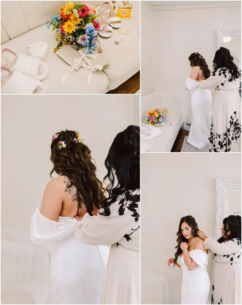 Snohomish Wedding Photographer GSquared Weddings In a room adorned with patterned wallpaper and a white couch, a woman in a white dress is being helped by another in a floral dress. Nearby, bridal accessories and colorful flowers, reminiscent of the vibrant blooms found in Machias, grace the table. Serving Seattle, Snohomish and Washington State