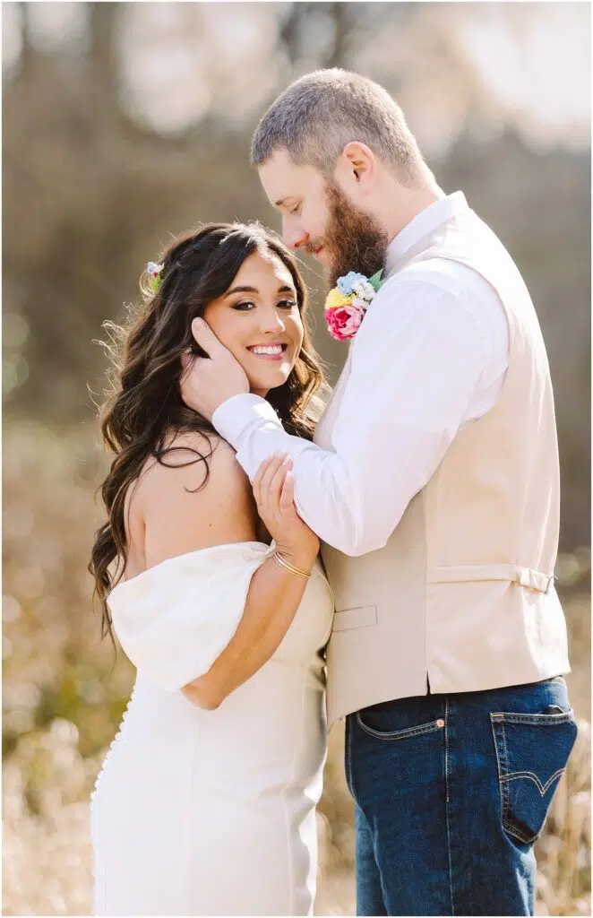 Snohomish Wedding Photographer GSquared Weddings A couple stands in Machias embracing happily The woman smiles at the camera in a white dress with floral accents in her hair The bearded man gently touches her face wearing a light vest over a white shirt Sunlight filters through the background capturing their joy Serving Seattle Snohomish and Washington State Snohomish Wedding Photographer GSquared Weddings A couple stands in Machias, embracing happily. The woman smiles at the camera in a white dress with floral accents in her hair. The bearded man gently touches her face, wearing a light vest over a white shirt. Sunlight filters through the background, capturing their joy. Serving Seattle, Snohomish and Washington State