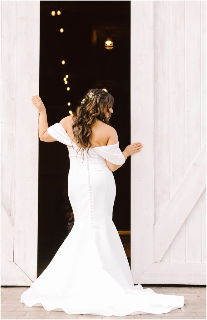 Snohomish wedding photographer gsquared weddings a bride in an off-shoulder white gown stands facing a large open barn door decorated with string lights Her long hair is styled with flowers and she looks back slightly in the serene machias countryside highlighting the gowns button details and flowing train Serving seattle snohomish and washington state Snohomish wedding photographer gsquared weddings a bride in an off shoulder white gown stands facing a large open barn door decorated with string lights Her long hair is styled with flowers and she looks back slightly in the serene machias countryside highlighting the gowns button details and flowing train Serving seattle snohomish and washington state