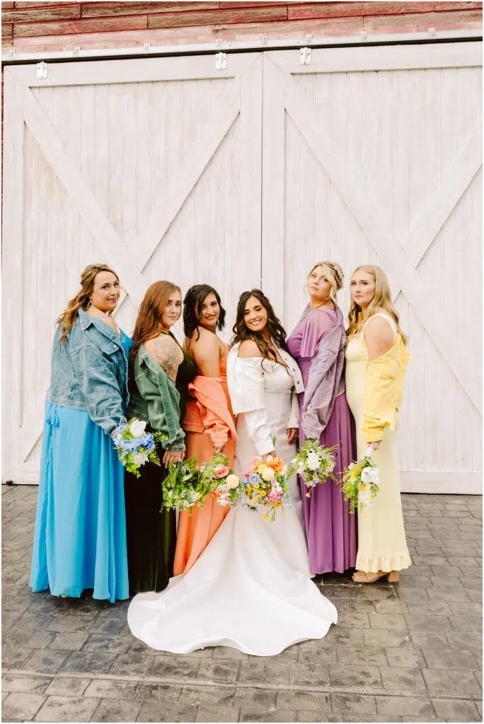 Snohomish Wedding Photographer GSquared Weddings A bride in a white dress stands with five bridesmaids in colorful dresses and denim jackets all gathered in front of Machiass iconic large white wooden doors Each holds a bouquet of flowers arranged in a row facing the camera smiling Serving Seattle Snohomish and Washington State Snohomish Wedding Photographer GSquared Weddings A bride in a white dress stands with five bridesmaids in colorful dresses and denim jackets, all gathered in front of Machiass iconic large white wooden doors. Each holds a bouquet of flowers, arranged in a row facing the camera, smiling. Serving Seattle, Snohomish and Washington State