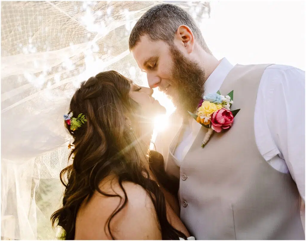 Snohomish Wedding Photographer GSquared Weddings Bride and groom embrace under a veil with the sun shining behind them creating a moment as enchanting as a Machias sunset The grooms beige vest complements his floral boutonniere while the brides hair blooms with flowers They gaze at each other lovingly Serving Seattle Snohomish and Washington State Snohomish Wedding Photographer GSquared Weddings Bride and groom embrace under a veil with the sun shining behind them, creating a moment as enchanting as a Machias sunset. The grooms beige vest complements his floral boutonniere, while the brides hair blooms with flowers. They gaze at each other lovingly. Serving Seattle, Snohomish and Washington State