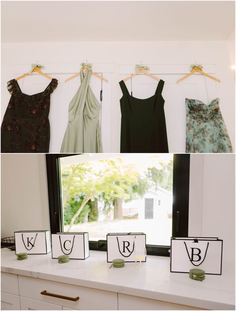 Snohomish Wedding Photographer GSquared Weddings Four dresses hang on a wall: a dark patterned one, a light green, a black, and floral—perfect for a summer wedding in Port Gamble. Below, four black-edged placards with the letters K, C, R, and B adorn the countertop with small green candles beside each. Serving Seattle, Snohomish and Washington State