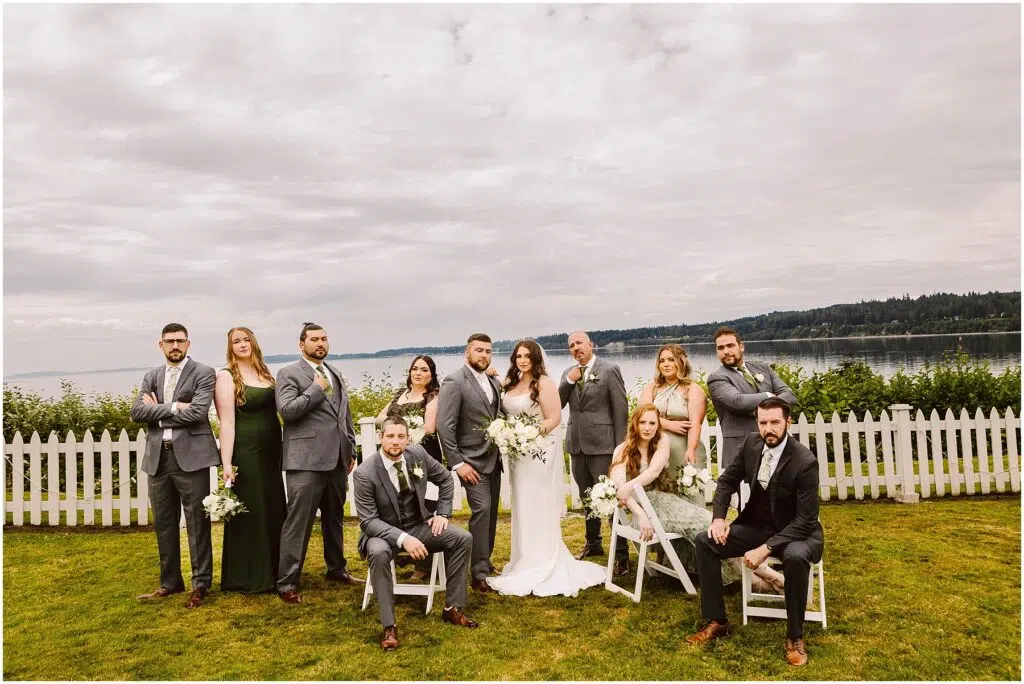 Snohomish Wedding Photographer GSquared Weddings A wedding party poses outdoors in front of a white fence capturing the charm of a Port Gamble summer wedding With scenic views of water and trees the group features seven men in gray suits and five women with bouquets while the bride and groom stand proudly in the center Serving Seattle Snohomish and Washington State Snohomish Wedding Photographer GSquared Weddings A wedding party poses outdoors in front of a white fence, capturing the charm of a Port Gamble summer wedding. With scenic views of water and trees, the group features seven men in gray suits and five women with bouquets, while the bride and groom stand proudly in the center. Serving Seattle, Snohomish and Washington State