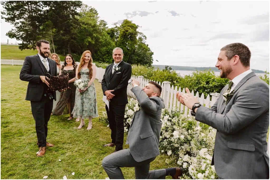 Snohomish Wedding Photographer GSquared Weddings A man in a gray suit kneels holding a ring box during a beautiful Port Gamble summer wedding Another man in a suit stands clapping surrounded by smiling bridesmaids in floral dresses and two other groomsmen They are outdoors with trees and a white fence in the background Serving Seattle Snohomish and Washington State Snohomish Wedding Photographer GSquared Weddings A man in a gray suit kneels, holding a ring box during a beautiful Port Gamble summer wedding. Another man in a suit stands clapping, surrounded by smiling bridesmaids in floral dresses and two other groomsmen. They are outdoors with trees and a white fence in the background. Serving Seattle, Snohomish and Washington State