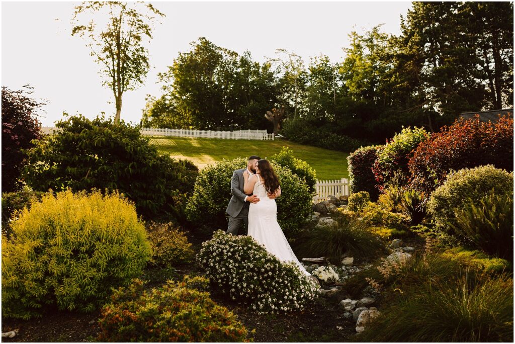 Snohomish wedding photographer gsquared weddings amidst a lush gardens vibrant greenery and colorful bushes a bride and groom share a kiss as the sun casts its warm glow over their summer wedding in port gamble Serving seattle snohomish and washington state Snohomish wedding photographer gsquared weddings amidst a lush gardens vibrant greenery and colorful bushes a bride and groom share a kiss as the sun casts its warm glow over their summer wedding in port gamble Serving seattle snohomish and washington state