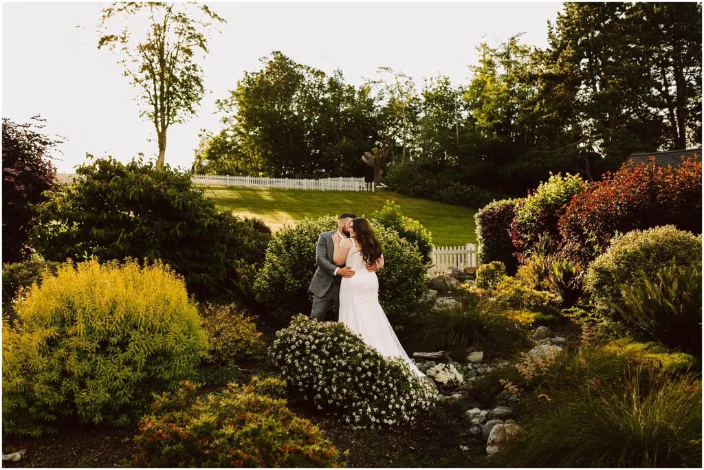 Snohomish Wedding Photographer GSquared Weddings Amidst a lush gardens vibrant greenery and colorful bushes a bride and groom share a kiss as the sun casts its warm glow over their summer wedding in Port Gamble Serving Seattle Snohomish and Washington State Snohomish Wedding Photographer GSquared Weddings Amidst a lush gardens vibrant greenery and colorful bushes, a bride and groom share a kiss as the sun casts its warm glow over their summer wedding in Port Gamble. Serving Seattle, Snohomish and Washington State