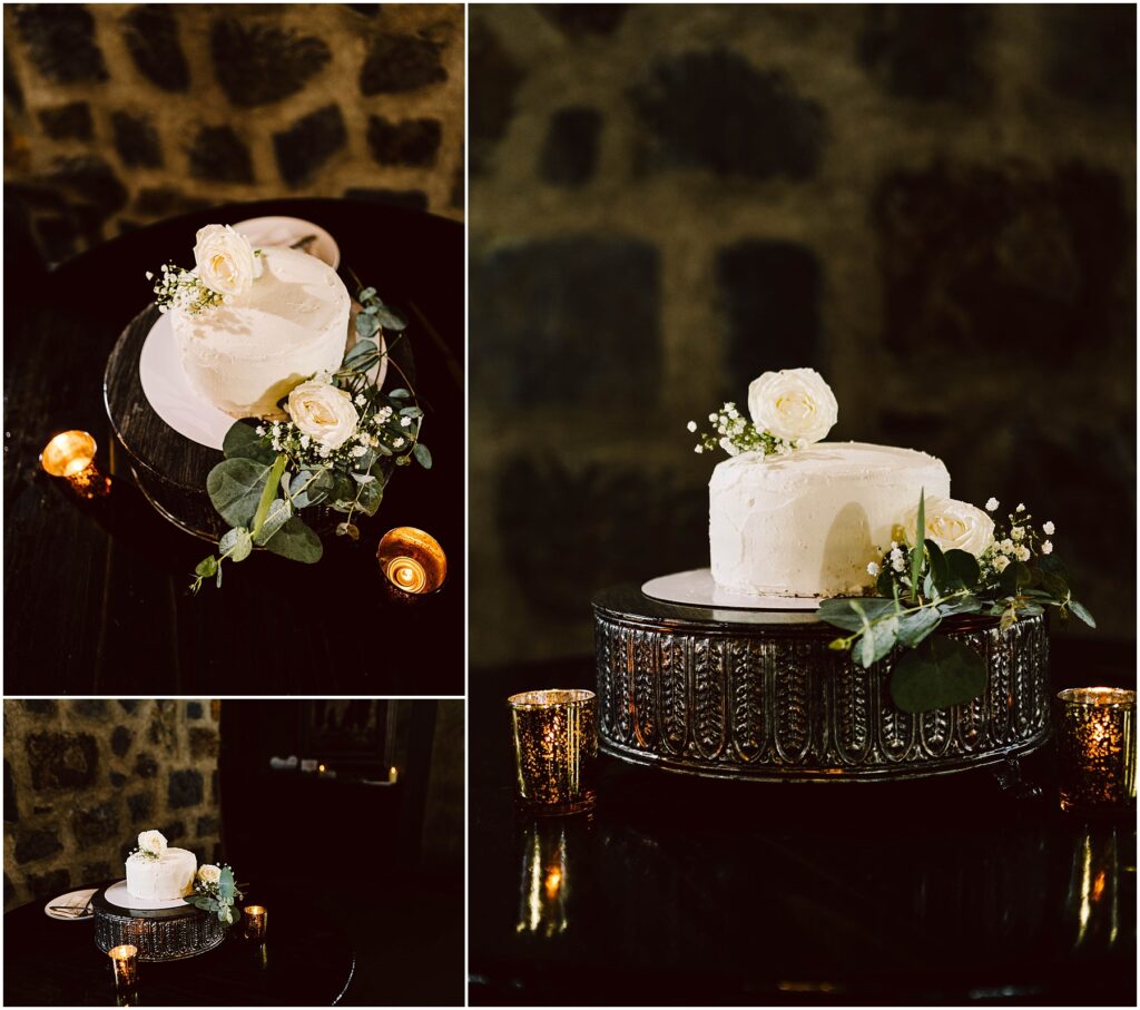 Snohomish Wedding Photographer GSquared Weddings A two-tiered white frosted cake adorned with white roses and greenery sits elegantly on an ornate stand, reminiscent of a winerys rustic charm. The cake is surrounded by small candles, set against a dark stone wall background. There are close-up and angled views of the cake. Serving Seattle, Snohomish and Washington State