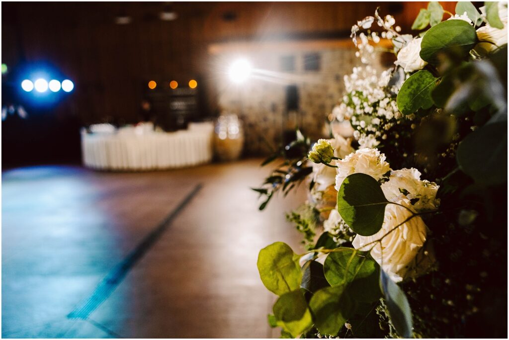 Snohomish Wedding Photographer GSquared Weddings A warmly lit event space with blurred ambient lights in the background. A bouquet of white and cream roses with greenery is prominently displayed in the foreground, evoking the charm of a winery setting. The atmosphere suggests a celebratory occasion. Serving Seattle, Snohomish and Washington State