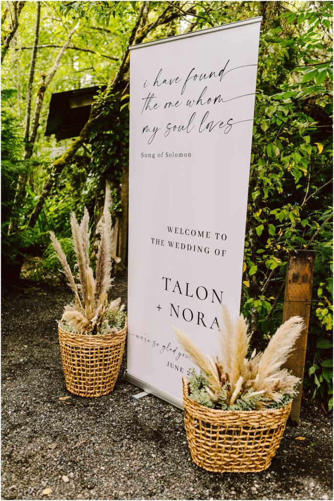 Snohomish Wedding Photographer GSquared Weddings In a picturesque Snohomish garden a wedding sign adorned with lush greenery welcomes guests to the Wedding of Talon + Nora A quote from Song of Solomon graces the sign while two baskets filled with pampas grass enhance its charming allure Serving Seattle Snohomish and Washington State Snohomish Wedding Photographer GSquared Weddings In a picturesque Snohomish garden, a wedding sign adorned with lush greenery welcomes guests to the Wedding of Talon + Nora. A quote from Song of Solomon graces the sign, while two baskets filled with pampas grass enhance its charming allure. Serving Seattle, Snohomish and Washington State