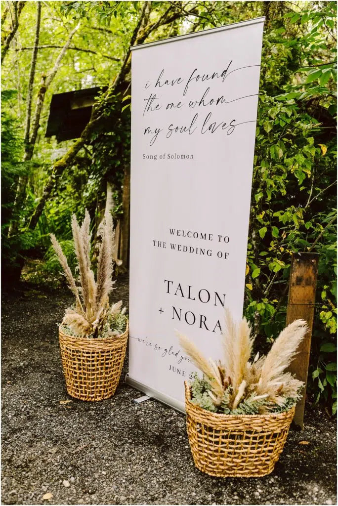 Snohomish Wedding Photographer GSquared Weddings In a picturesque Snohomish garden a wedding sign adorned with lush greenery welcomes guests to the Wedding of Talon + Nora A quote from Song of Solomon graces the sign while two baskets filled with pampas grass enhance its charming allure Serving Seattle Snohomish and Washington State Snohomish Wedding Photographer GSquared Weddings In a picturesque Snohomish garden, a wedding sign adorned with lush greenery welcomes guests to the Wedding of Talon + Nora. A quote from Song of Solomon graces the sign, while two baskets filled with pampas grass enhance its charming allure. Serving Seattle, Snohomish and Washington State