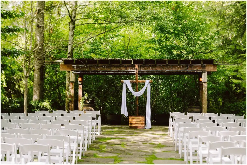 Snohomish Wedding Photographer GSquared Weddings An outdoor wedding setup in Snohomish features rows of white chairs facing a wooden arbor draped with white fabric The lush green trees and foliage create a serene forest setting under clear daylight perfect for a tranquil celebration Serving Seattle Snohomish and Washington State Snohomish Wedding Photographer GSquared Weddings An outdoor wedding setup in Snohomish features rows of white chairs facing a wooden arbor draped with white fabric. The lush green trees and foliage create a serene forest setting under clear daylight, perfect for a tranquil celebration. Serving Seattle, Snohomish and Washington State