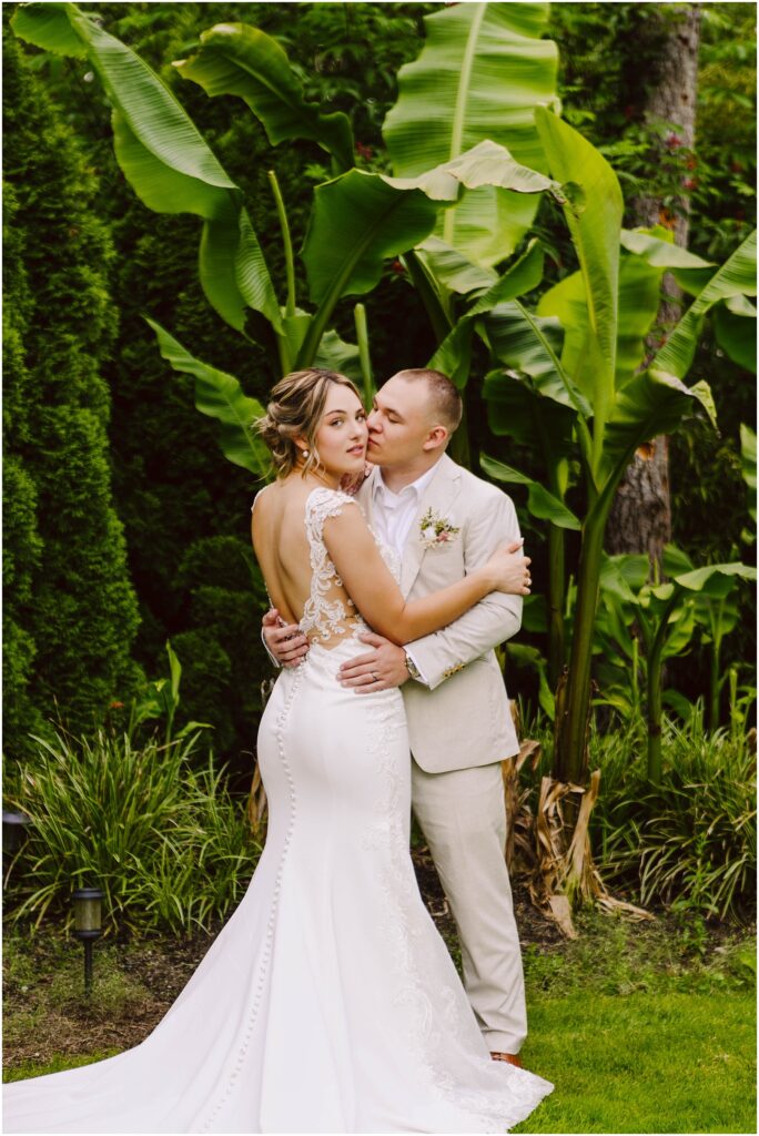 Snohomish Wedding Photographer GSquared Weddings In a lush Snohomish garden the bride in a white lace gown and groom in a light suit embrace among large green leaves The bride looks serenely at the camera while the groom gazes lovingly at her surrounded by vibrant tropical foliage Serving Seattle Snohomish and Washington State Snohomish Wedding Photographer GSquared Weddings In a lush Snohomish garden, the bride in a white lace gown and groom in a light suit embrace among large green leaves. The bride looks serenely at the camera while the groom gazes lovingly at her, surrounded by vibrant tropical foliage. Serving Seattle, Snohomish and Washington State