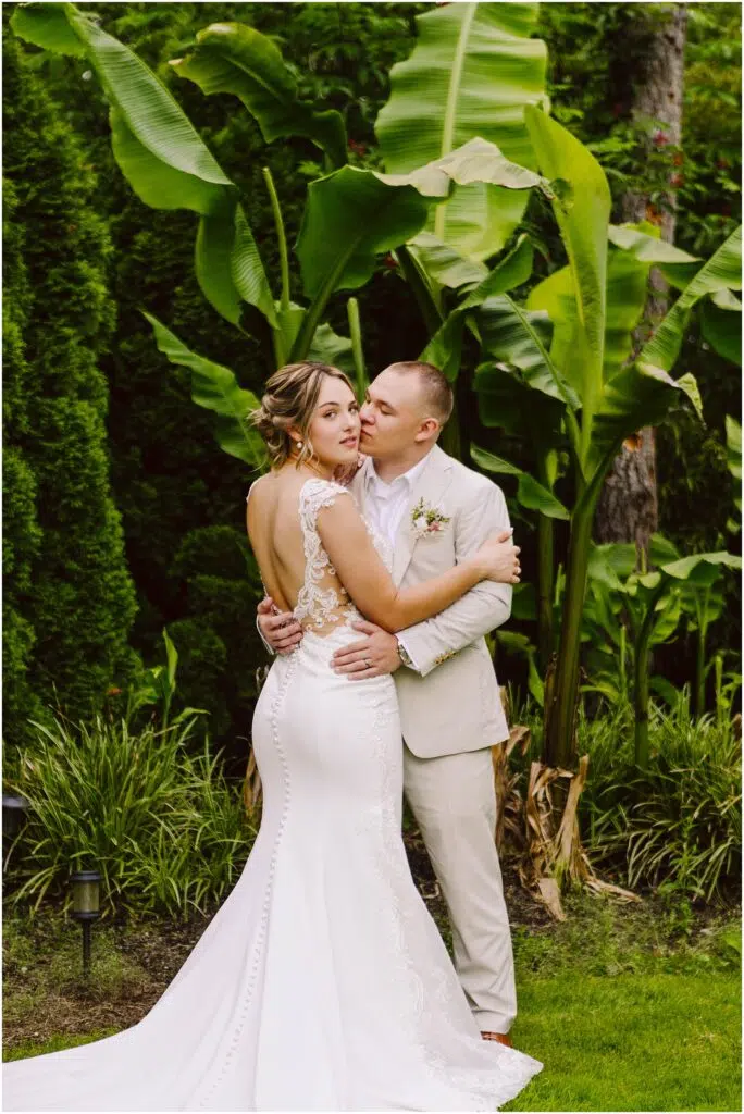 Snohomish Wedding Photographer GSquared Weddings In a lush Snohomish garden the bride in a white lace gown and groom in a light suit embrace among large green leaves The bride looks serenely at the camera while the groom gazes lovingly at her surrounded by vibrant tropical foliage Serving Seattle Snohomish and Washington State Snohomish Wedding Photographer GSquared Weddings In a lush Snohomish garden, the bride in a white lace gown and groom in a light suit embrace among large green leaves. The bride looks serenely at the camera while the groom gazes lovingly at her, surrounded by vibrant tropical foliage. Serving Seattle, Snohomish and Washington State