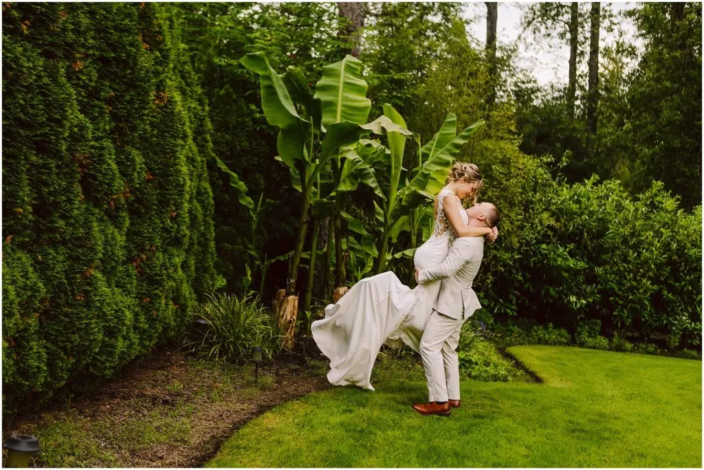 Snohomish Wedding Photographer GSquared Weddings In a lush Snohomish garden a groom in a light suit lifts the bride in her white dress amid vibrant green foliage and banana plants Their joy is palpable as she gazes at him lovingly while being held Serving Seattle Snohomish and Washington State Snohomish Wedding Photographer GSquared Weddings In a lush Snohomish garden, a groom in a light suit lifts the bride in her white dress amid vibrant green foliage and banana plants. Their joy is palpable as she gazes at him lovingly while being held. Serving Seattle, Snohomish and Washington State