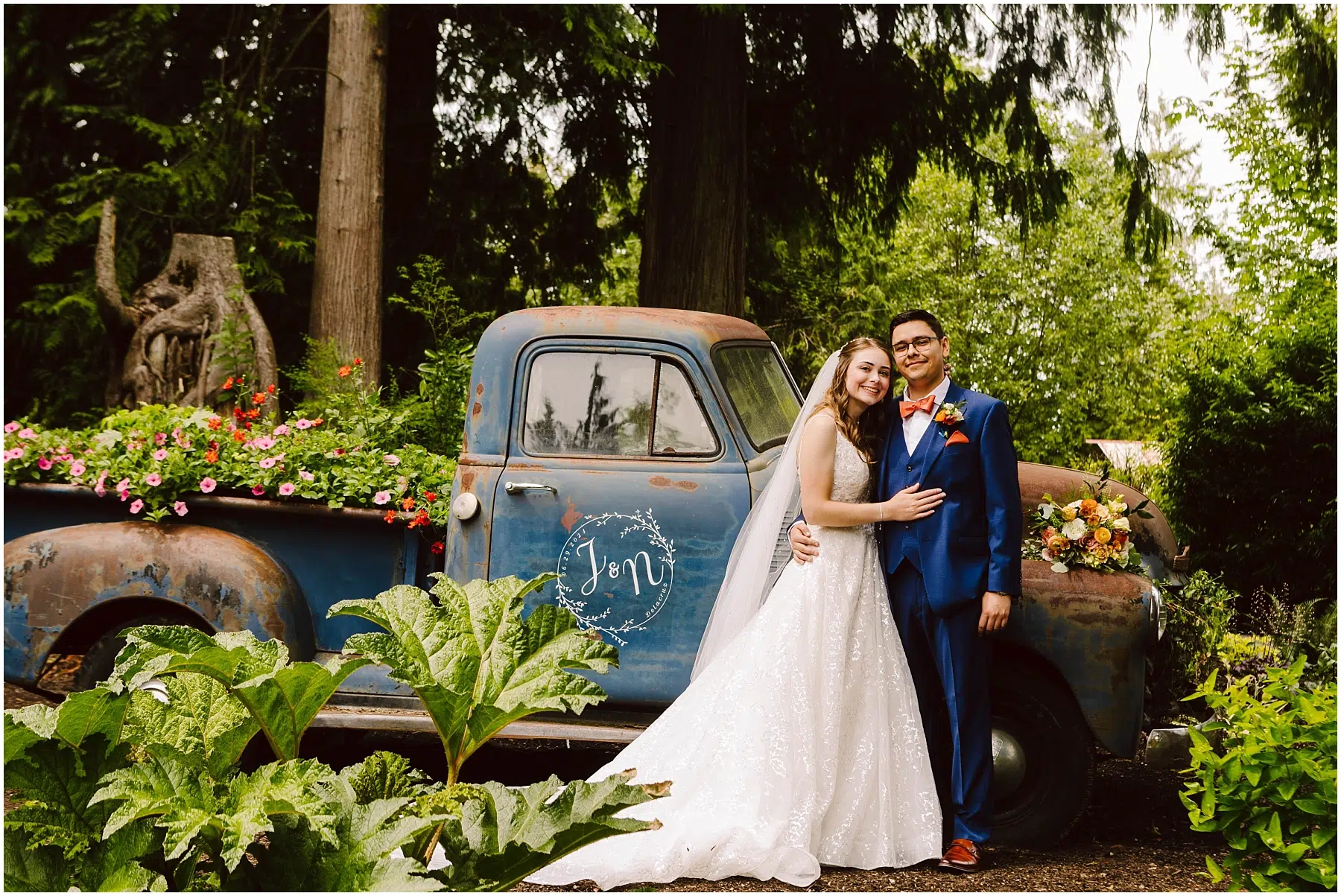 Stanwood Backyard Wedding Snohomish Wedding Photographer GSquared Weddings In a charming Stanwood setting, a bride in a white dress and a groom in a blue suit stand happily in front of a vintage blue pickup truck adorned with flowers. The truck is parked amid the lush beauty of their backyard garden, creating the perfect backdrop for their wedding day. Serving Seattle, Snohomish and Orlando