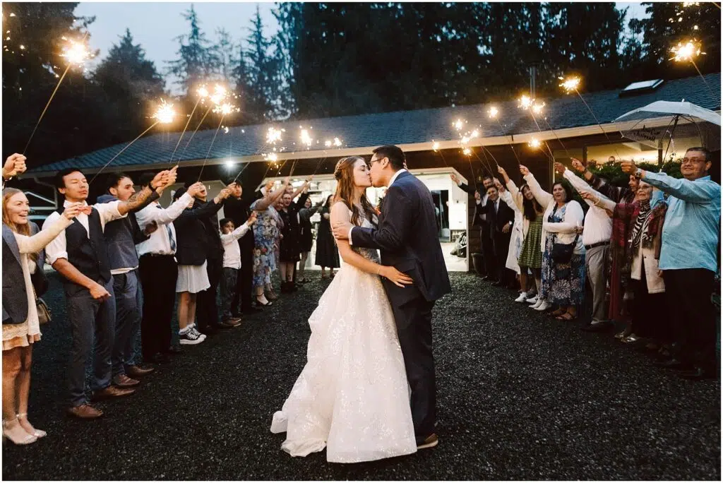 Snohomish Wedding Photographer GSquared Weddings A bride and groom share a kiss under the night sky during their backyard wedding surrounded by guests holding sparklers The scene is festive with an arch of light formed by the guests and a backdrop of trees and a lit building Serving Seattle Snohomish and Washington State Snohomish Wedding Photographer GSquared Weddings A bride and groom share a kiss under the night sky during their backyard wedding, surrounded by guests holding sparklers. The scene is festive, with an arch of light formed by the guests and a backdrop of trees and a lit building. Serving Seattle, Snohomish and Washington State