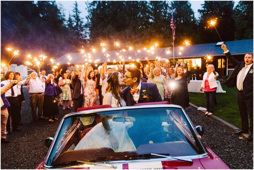 Snohomish Wedding Photographer GSquared Weddings A bride and groom kiss while sitting in a red convertible during a magical nighttime backyard wedding celebration Guests stand around holding sparklers with a lit building visible in the background amidst the trees Serving Seattle Snohomish and Washington State Snohomish Wedding Photographer GSquared Weddings A bride and groom kiss while sitting in a red convertible during a magical nighttime backyard wedding celebration. Guests stand around holding sparklers, with a lit building visible in the background amidst the trees. Serving Seattle, Snohomish and Washington State