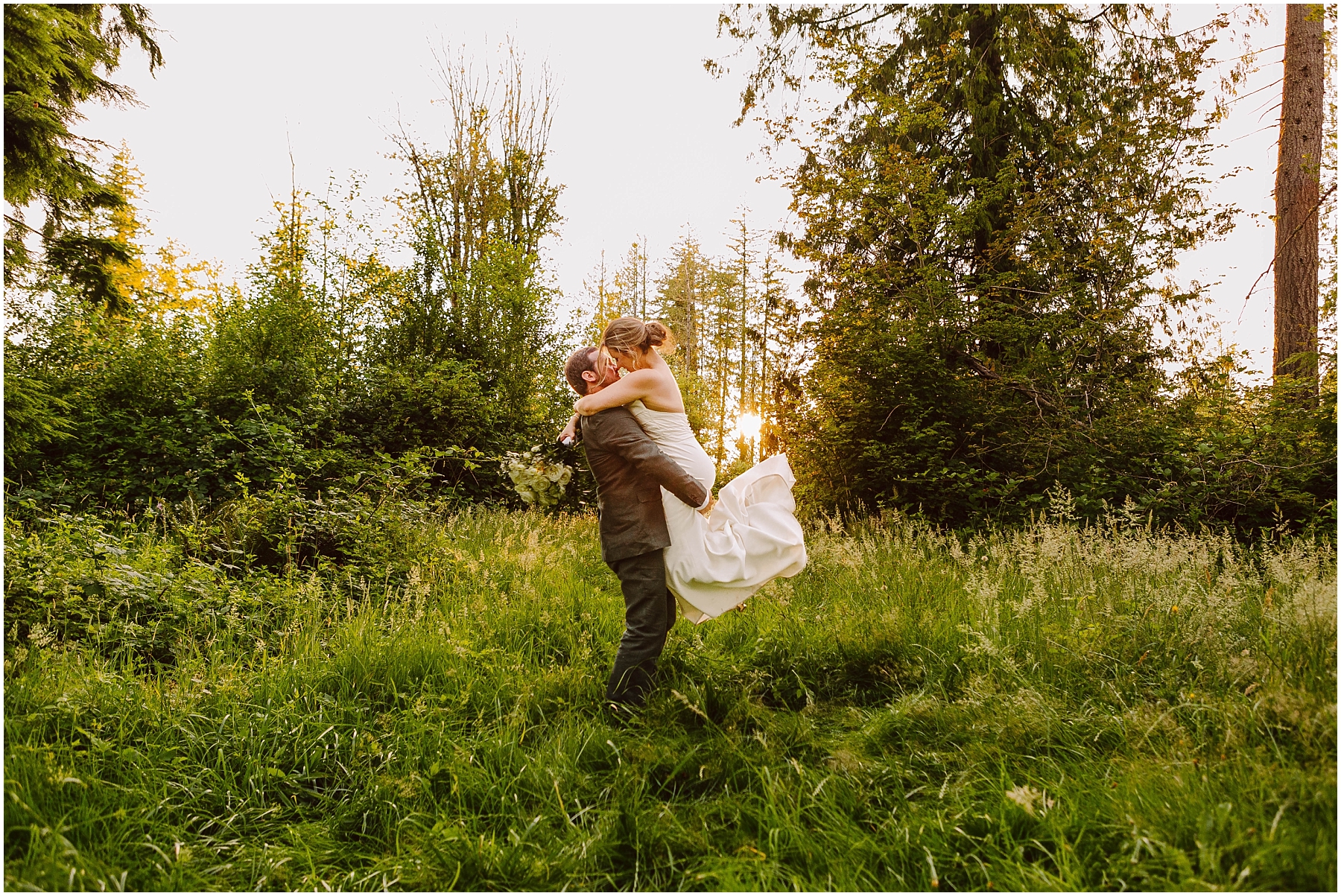 GSquared Weddings Photography A groom lifts and embraces his bride in a grassy, sunlit clearing surrounded by tall green trees in Snohomish County, both smiling and joyful on their wedding day. GSquared Weddings | 47.9129° N, 122.0982° W | Serving Snohomish, Seattle , Orlando & Beyond