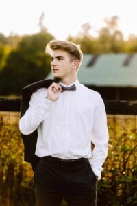 Young man in a white dress shirt and bow tie holding a black jacket over his shoulder