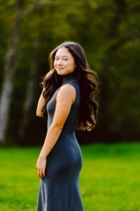 Young woman with long dark hair in a sleeveless gray dress on green grass looking over her shoulder