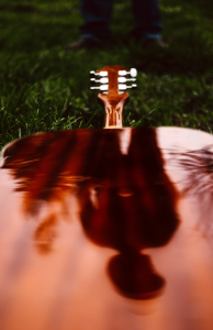 Acoustic guitar lying on the grass its polished surface reflecting a person standing nearby