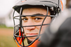 Close up of a young athlete in a black and orange helmet with a faceguard looking at the camera