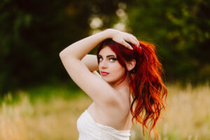 Senior with long red hair in a white strapless top holding her hair up posing outdoors