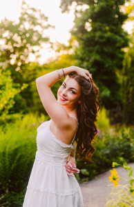 Smiling senior in a white dress holding her hair with one hand on a lush garden path