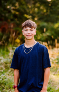 Teenage boy in a navy t shirt with a silver chain and red watch outdoors