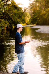Young person in a baseball cap fishing at the rivers edge