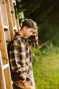 Teenage boy in a plaid shirt leaning on a wooden wall touching his hair