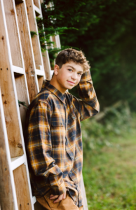 Teenage boy in a plaid shirt standing by a wooden fence