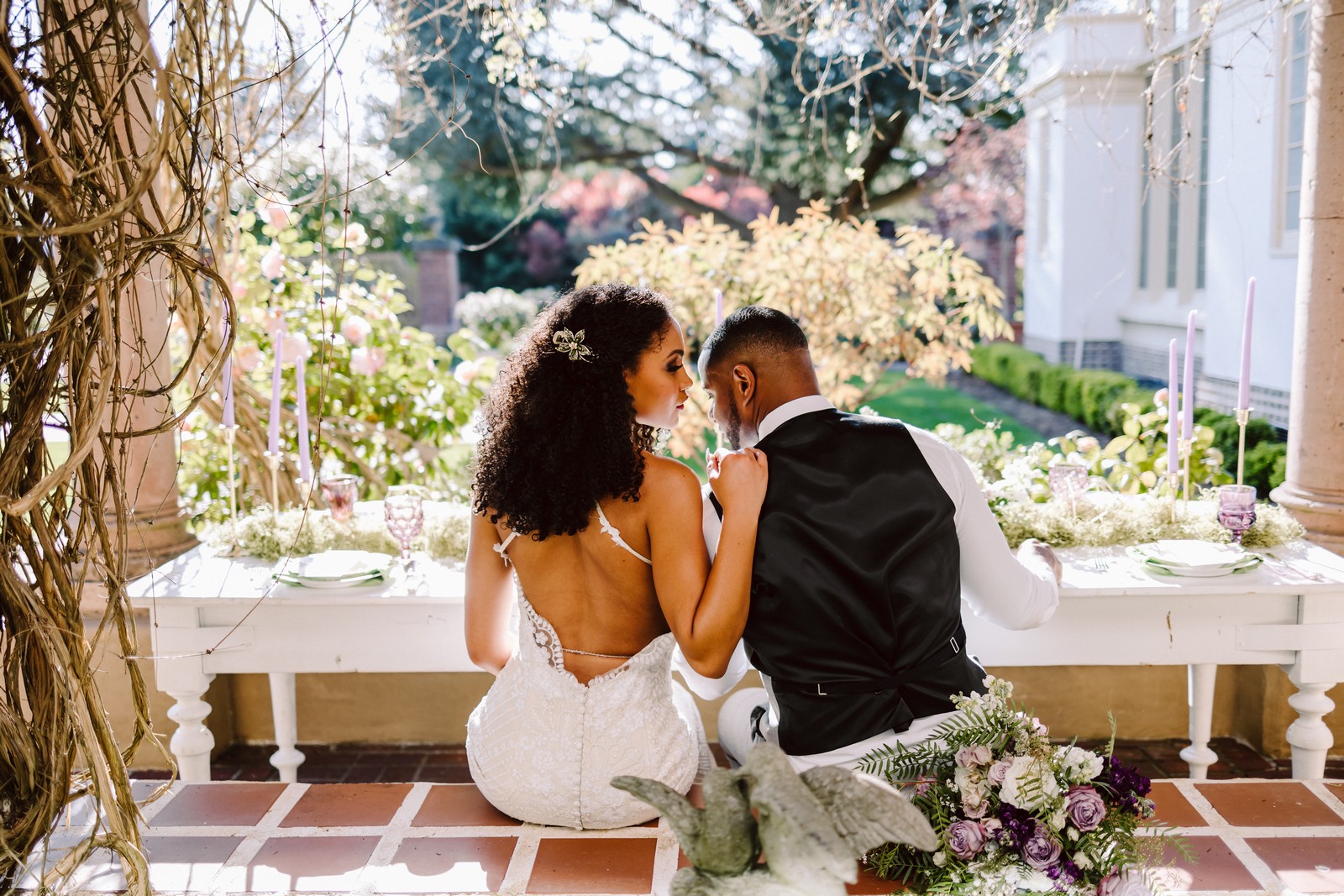 KMG6988 micro wedding couple at lairmont manor bellingham sitting together at a sweetheart table snuggled up black groom in a black vest and black bride in an open back dress a bouquet sits near the groom on the stone wall. Intentional seattle and snohomish wedding planning