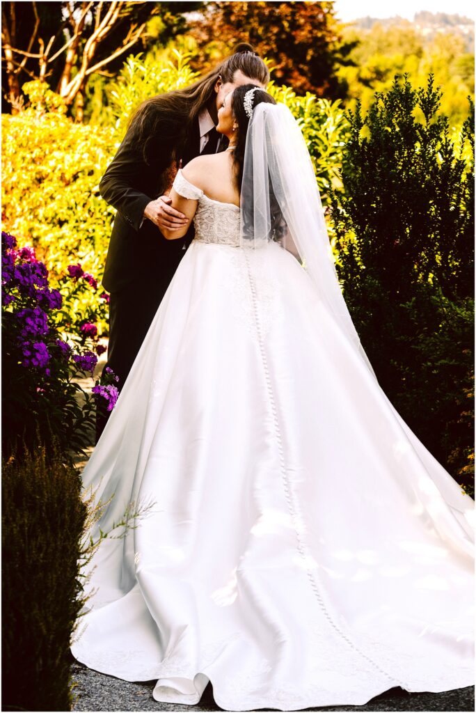 Bride and groom kissing in a sunlit garden bride in a white wedding gown and veil among colorful flowers