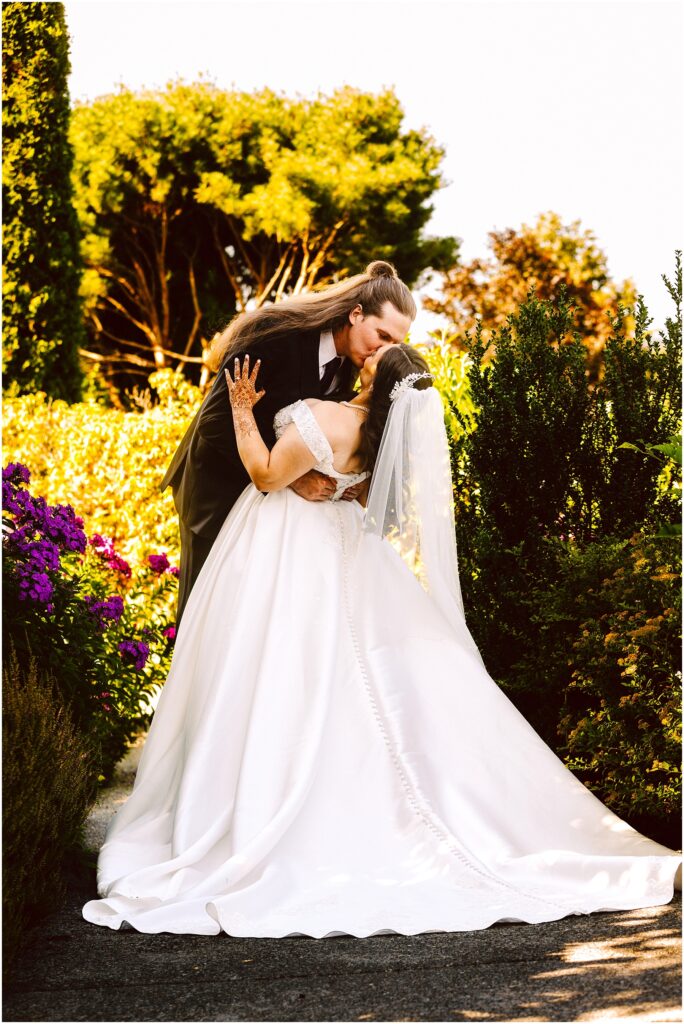 Bride and groom sharing a kiss outdoors in a garden bride in a white gown and veil groom in a dark suit