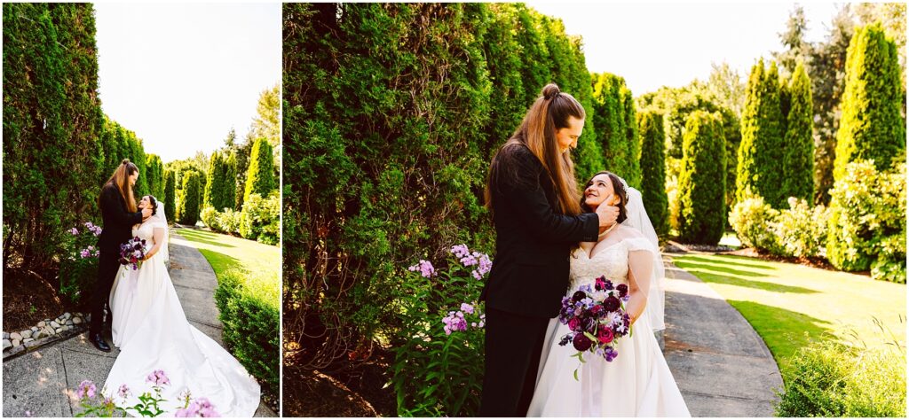 Bride in white gown and veil holds purple bouquet as partner in black suit tenderly holds her face outdoors on a garden path
