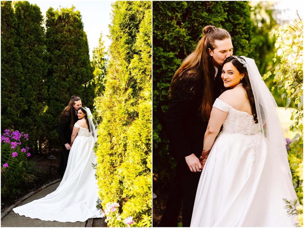 Bride in a white wedding gown and veil with groom kissing her head in a garden