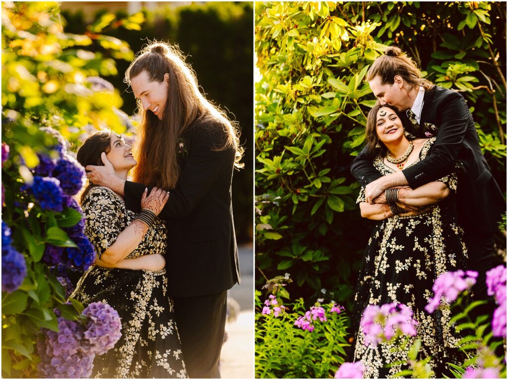 A tall man with long hair in a black suit embraces a woman in an ornate black and gold embroidery dress smiling among purple hydrangeas in a sunlit garden left panel