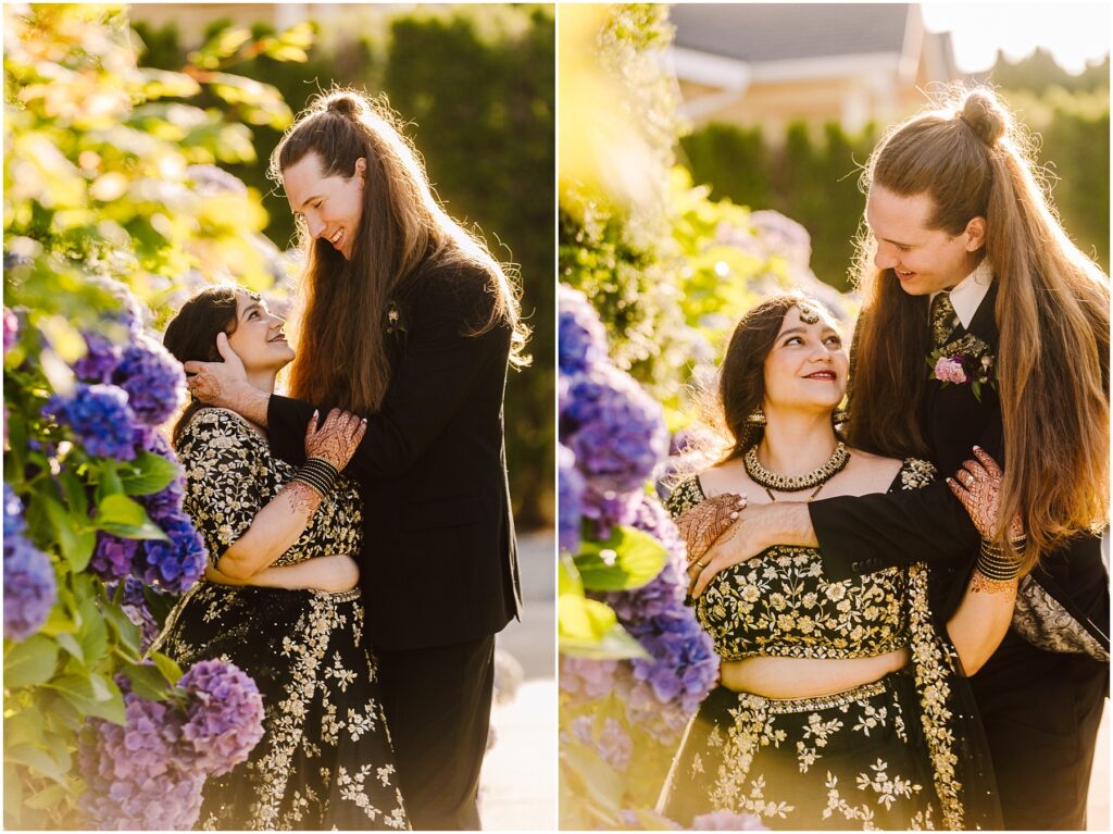 Couple embracing in a sunlit garden among purple hydrangeas woman in a black and gold embroidery outfit man in a black suit with long hair tied back