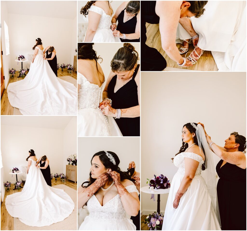 Bride in a white wedding gown standing in a bright room while a woman in black helps fasten the back of her dress bouquets arranged on the floor nearby