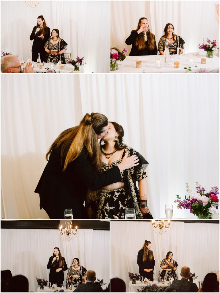 Man with microphone speaking at a decorated wedding table while a woman in a jeweled black outfit smiles beside him