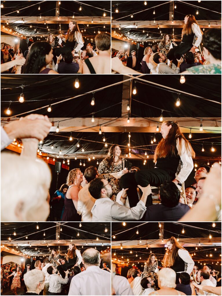 Joyful wedding reception as guests hoist a person on a chair amid warm string lights under a decorated ceiling