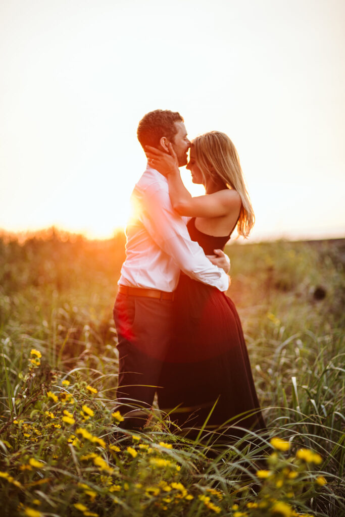 Couple embracing and kissing in a wildflower field at golden sunset surrounded by yellow flowers and tall grass