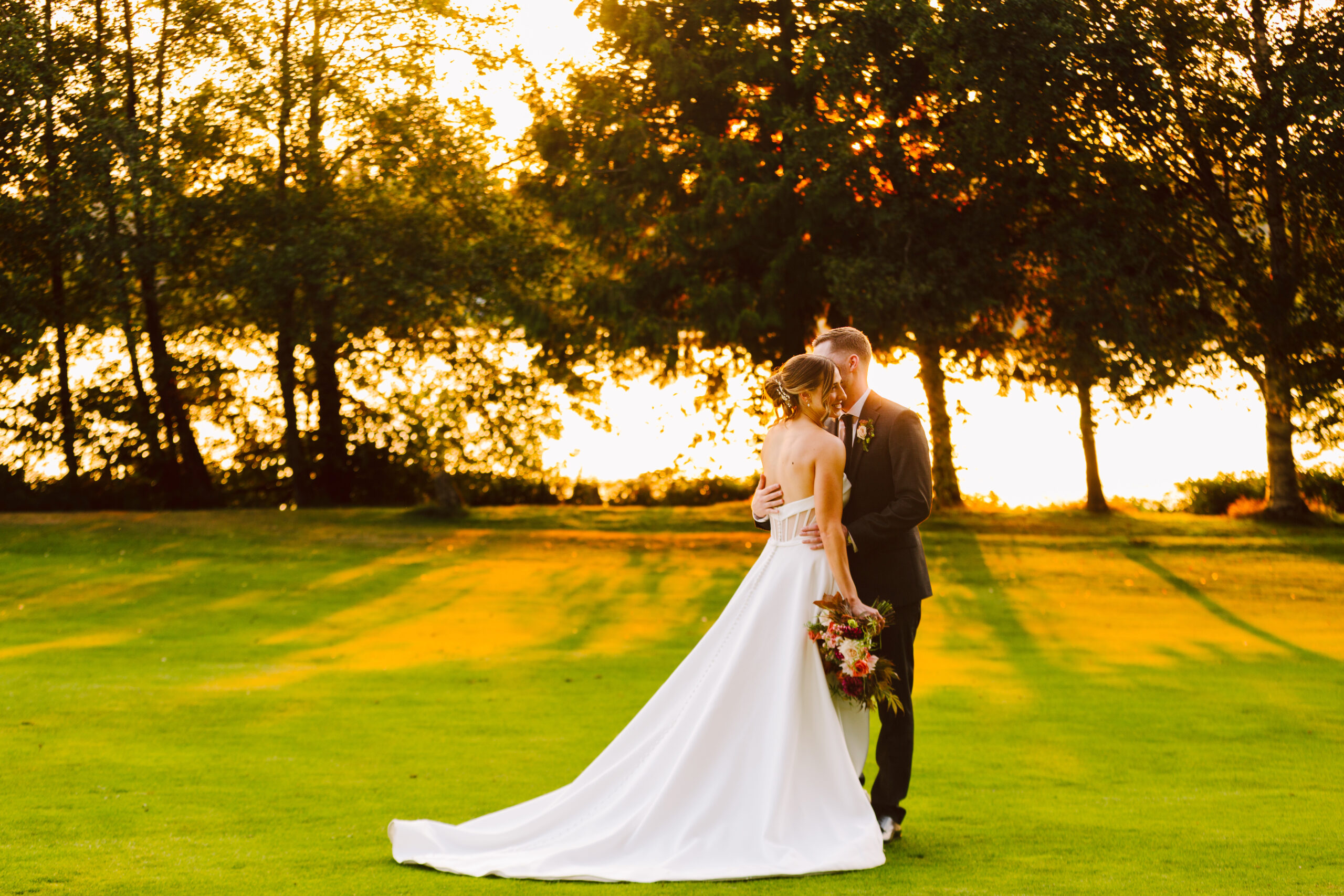 nile shrine golf course wedding bride and groom hugging in a orange and red glowing sunset by trees and a pond